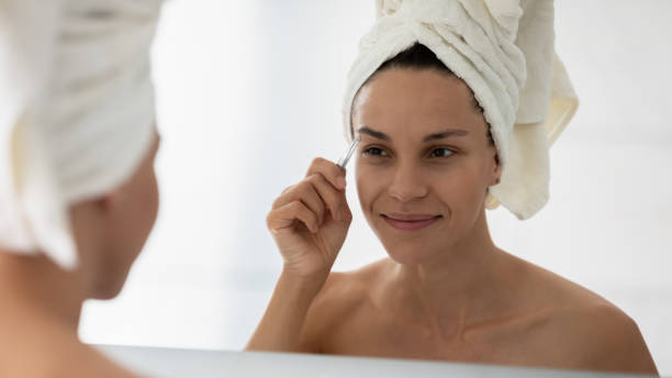 istock Closeup woman face reflected in mirror holding tweezers plucks eyebrows 1216575373