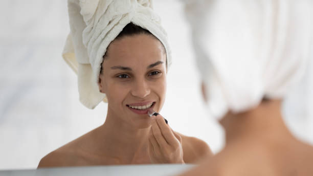 Woman looking in mirror applying long-lasting lipstick on lips