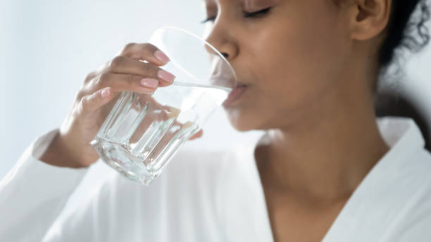 imagen de primer plano mujer africana sosteniendo vidrio bebiendo agua quieta - agua potable fotos fotografías e imágenes de stock