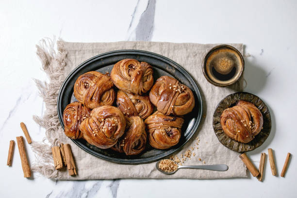 Swedish cinnamon sweet buns Traditional Swedish cinnamon sweet buns Kanelbulle on vintage tray, cup of coffee, cinnamon sticks, blossom branches on linen cloth over white marble background. Flat lay, space. kanelbulle stock pictures, royalty-free photos & images