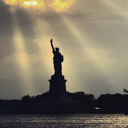 A silhouette of statue of Liberty with crepuscular rays behind.