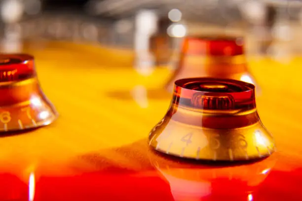 selective focus on the amber knob located on the top of a flamed cherry colored electric guitar