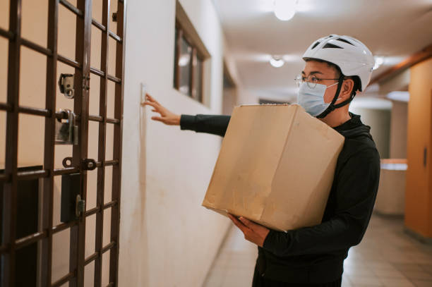 an asian chinese delivery man with helmet and surgical mask press door bell for grocery delivery - service bell fotos imagens e fotografias de stock