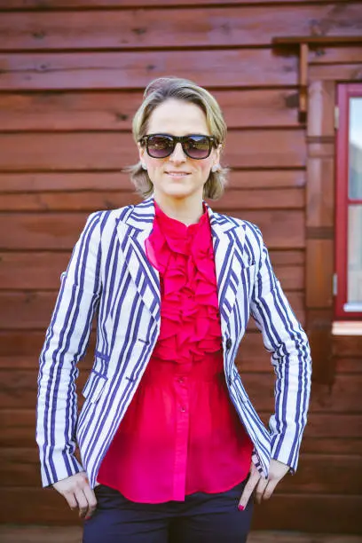 June 30, 2013 - Norway:Beautiful young women dressed up in formalwear - elegant, confident, relaxed - smiling keeping hands in pockets, wearing sunglasses standing in front of wooden wall