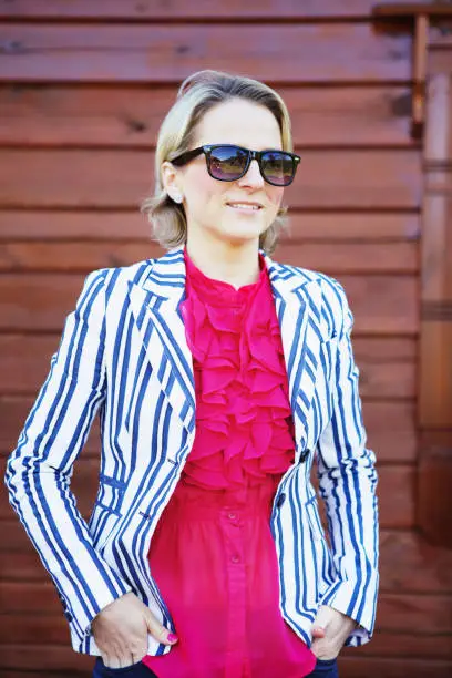 June 30, 2013 - Norway:pretty slim confident, smiling, blond business woman in white jacket, ed blouse, sunglasses looking away standing near plank wall outdoors