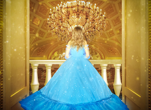 Beautiful princess in blue long shiny dress on the luminous yellow chandelier background