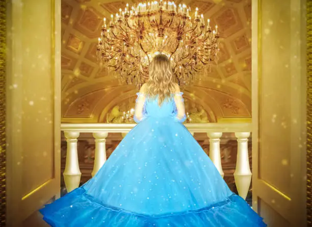 Beautiful princess in blue long shiny dress on the luminous yellow chandelier background