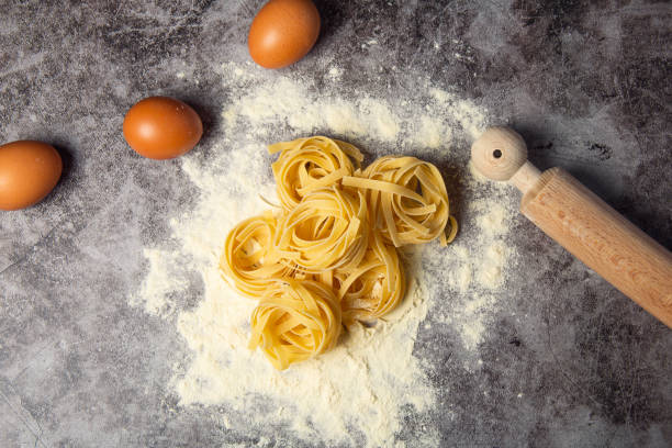 istock Fresh italian egg pasta nests, tagliatelle, isolated on dark marble background with eggs, flour and rolling pin. 1216588446