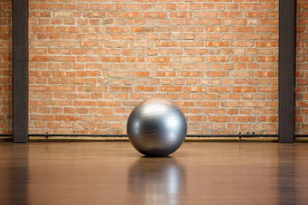 A silver fitball lies on the floor in a fitness room with a brick wall