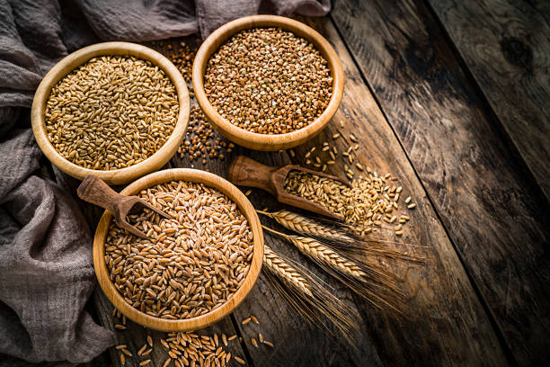 Dietary fiber: high angle view of three bowls filled with wholegrain buckwheat, wheat grains and spelt shot on rustic kitchen table. The composition is at the left of an horizontal frame leaving useful copy space for text and/or logo at the right. Predominant color is brown. XXXL 42Mp studio photo taken with SONY A7rII and Zeiss Batis 40mm F2.0 CF