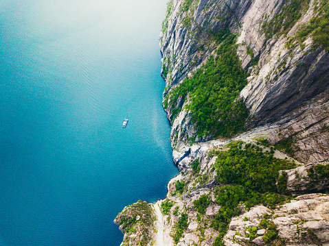 Drone photo of  turquoise colored sea, high cling and a boat sailing at the Lysefjord in South Norway