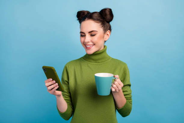 Photo of attractive teen lady hold beverage cup enjoy morning freelance work browsing telephone blog wear warm green turtleneck pullover isolated blue color background Photo of attractive teen lady hold beverage cup enjoy morning, freelance work browsing telephone blog wear warm green turtleneck pullover isolated blue color background topknot stock pictures, royalty-free photos & images