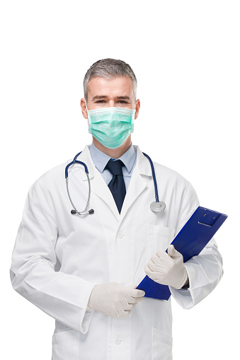 Doctor wearing lab coat, surgical mask, gloves and stethoscope holding a patient file or medical notes on a clipboard in his hands and he  looks at the camera isolated on white