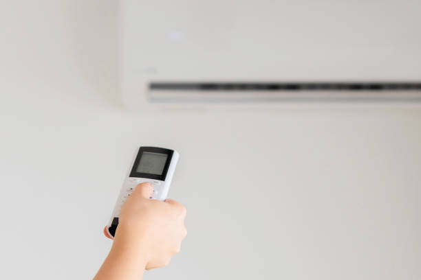 istock Brunette woman holding remote controller from air conditioner inside the room. Back view. 1216606647