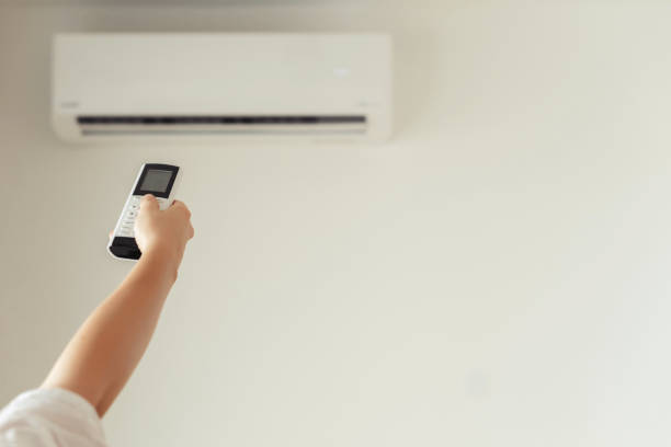 istock Brunette woman holding remote controller from air conditioner inside the room. Back view. 1216606697