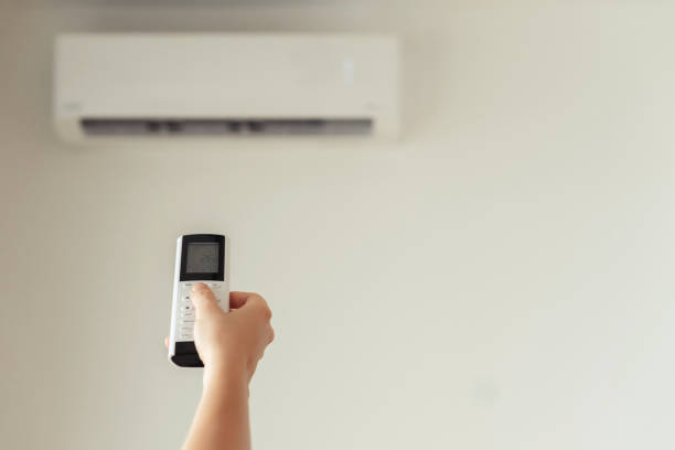 istock Brunette woman holding remote controller from air conditioner inside the room. Back view. 1216606699