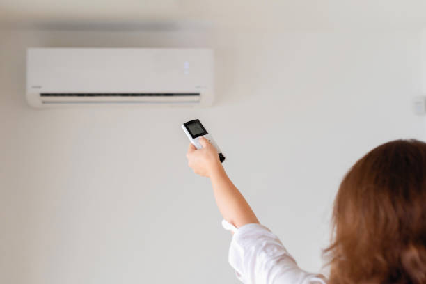 istock Brunette woman holding remote controller from air conditioner inside the room. Back view. 1216606740