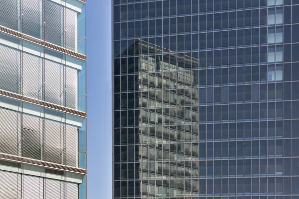 bürogebäude mit reflexionen in glasfassade eines anderen gebäudes - glass wall office building abstract stock-fotos und bilder