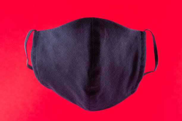 istock Handmade protective mask. Antivirus mask made from cotton. Black stylish face mask during a pandemic virus COVID-19. Face protective mask on a red background 1216612073
