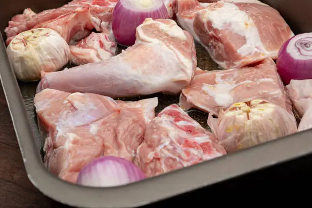 Raw meat of suckling lamb (suckling lamb). Prepared on a roasting tray (with garlic and red onion).