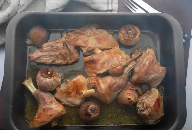 Roast meat of suckling lamb (suckling lamb). Fresh from the oven and smoking. Prepared on a roasting tray (with garlic and red onion).