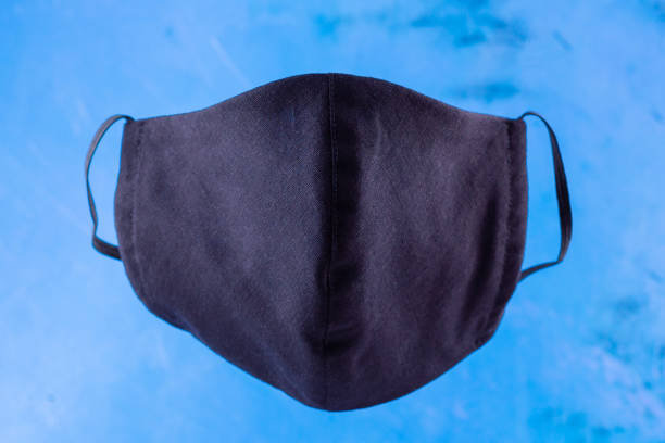 istock Handmade protective mask. Antivirus mask made from cotton. Black stylish face mask during a pandemic virus COVID-19. Face protective mask on a blue background 1216616099