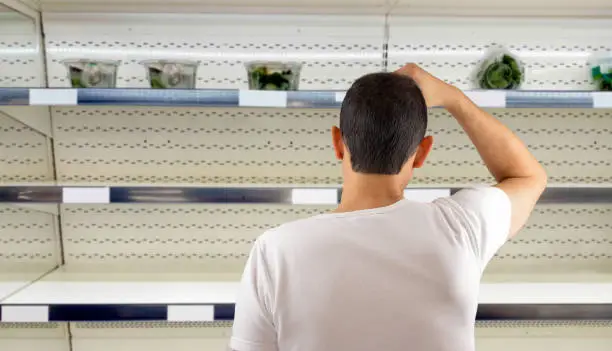 Photo of man at empty shelves in shop scratches in nape