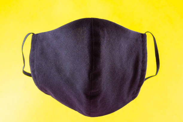 istock Handmade protective mask. Antivirus mask made from cotton. Black stylish face mask during a pandemic virus COVID-19. Face protective mask on a yellow background 1216618536