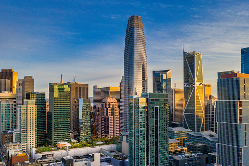 An aerial view of the financial district in San Francisco California as the sun comes up. Sun bounces off the skyscrapers. Salesforce elevate park is visible.