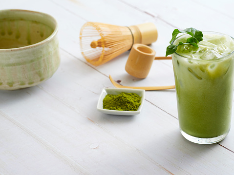 Homemade Iced Matcha Green Tea with bamboo whisk, green tea powder on white wooden.