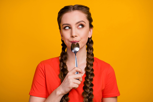 Photo of pretty teenager lady hold metal spoon in mouth desire, dinner look dreamy empty space think of tasty food wear casual red t-shirt isolated vivid yellow color background