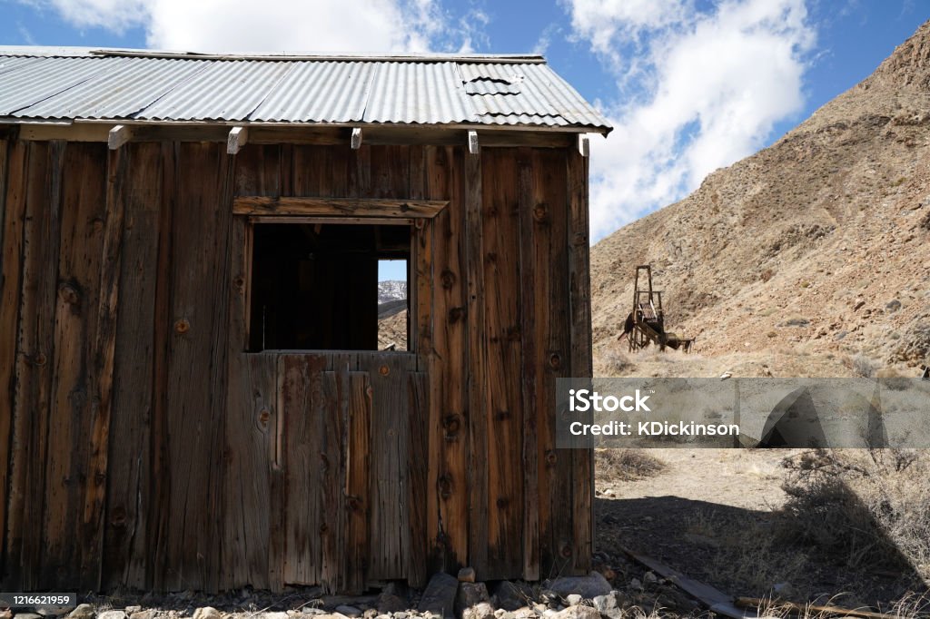An abandonded building on a former mining site. A view of the mountains can be seen through a window of an abandonded structure with mining equipment in the background. Abandoned Stock Photo