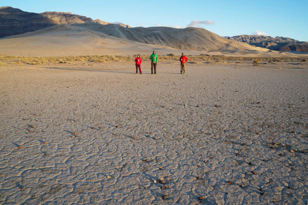 Three people stand on the desert playa in front of Eureka Dunes stock photo