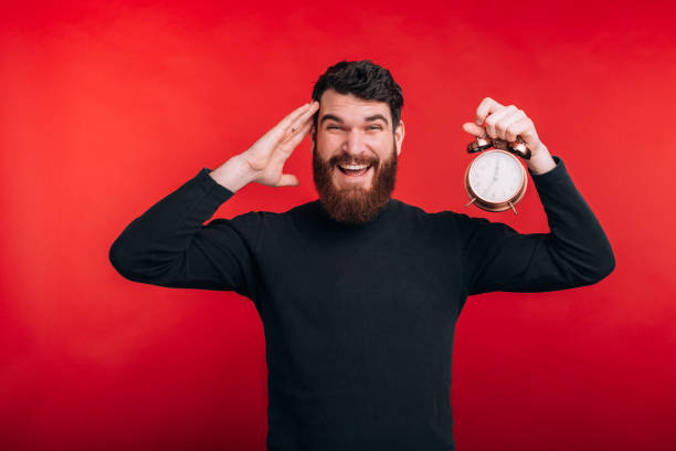 istock amazed bearded man standing over red background and holding alarm clockd 1216622565