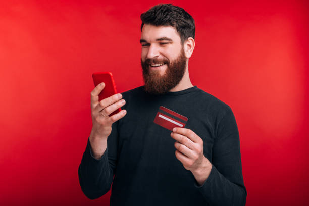 istock smiling young man with beard looking at smartphone and holding credit card 1216622705