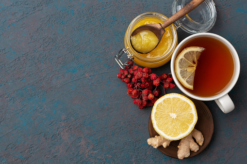 Season illness prevention background. Vitamin tea with lemon, ginger and honey with rowanberry on dark blue wooden background.