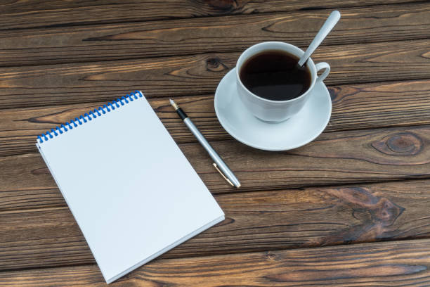 istock Cup with coffee and a blank notebook with pen on a wooden table. White blank mock up page 1216631511