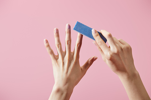 Vista parcial de la mujer haciendo manicura con tampón de uñas aislado en rosa photo