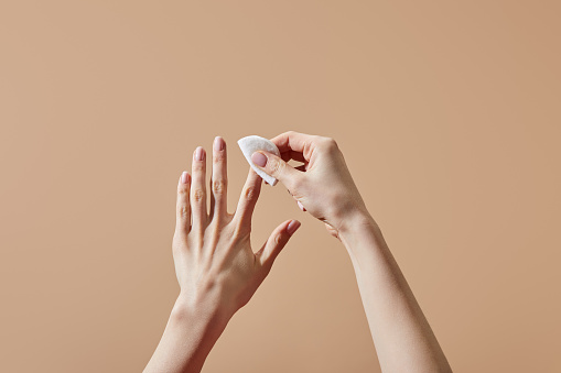 Vista parcial de la mujer quitando esmalte de uñas con almohadilla de algodón aislada en beige photo