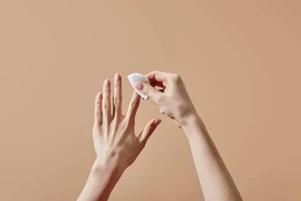 Partial view of woman removing nail polish with cotton pad isolated on beige