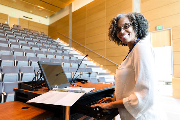 Smiling female university professor pauses work to pose for photo The cheerful, mature adult female university professor pauses in her class preparation to smile for the camera.  She is using the audio visual equipment. continuing education stock pictures, royalty-free photos & images