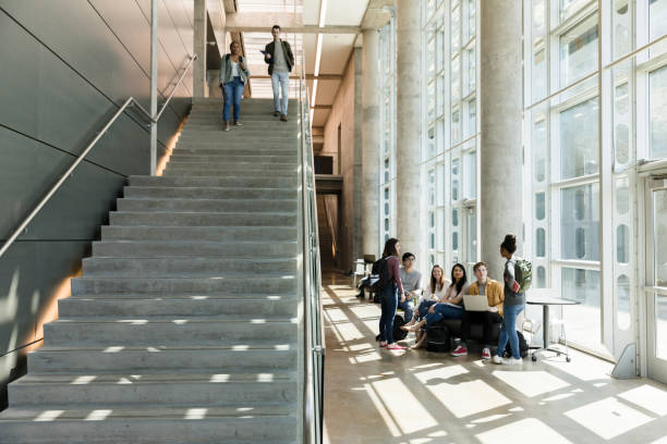 College students descend indoor staircase Male and female college friends walk down a long staircase on campus. Other students are studying in a common area. campus stock pictures, royalty-free photos & images