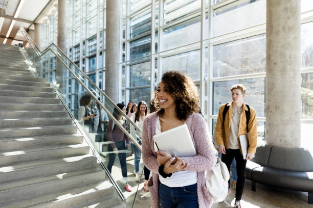Excited female college student walking to class An excited mixed race female college student smiles as she walks to her next class. Students are walking in the background. community college stock pictures, royalty-free photos & images