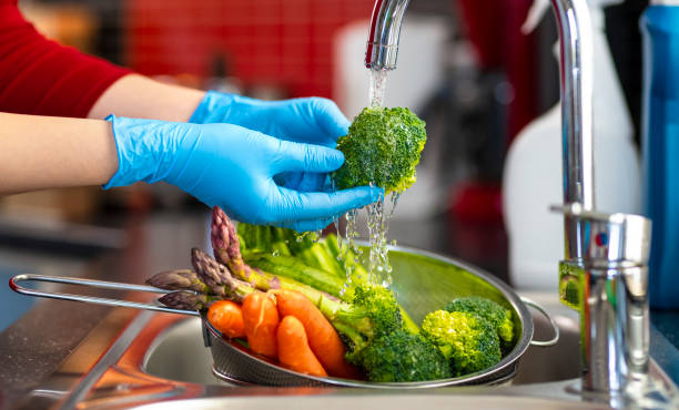 Disinfecting groceries during COVID-19 coronavirus outbreak Woman washing vegetables on kitchen counter. surgical glove stock pictures, royalty-free photos & images