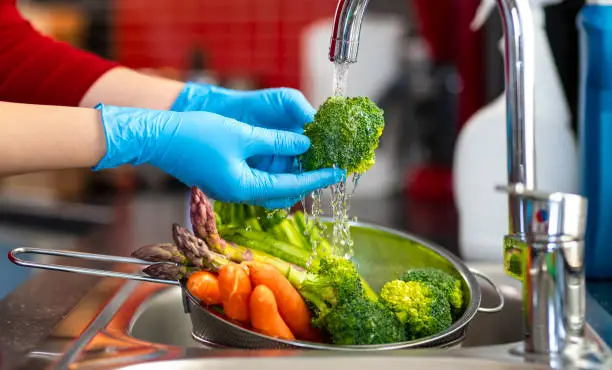 Woman washing vegetables on kitchen counter.