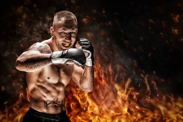 Photo of Mixed martial artist posing against the backdrop of fire and smoke. Concept of mma, ufc, thai boxing, classic boxing.