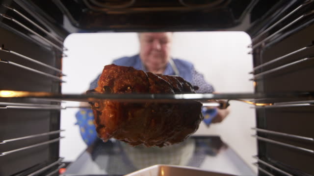 Woman cooking rotisserie spit roasted pork meat in oven at home
