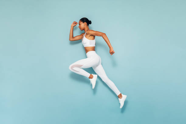 sports woman running in studio. full length shot of young female exercising over blue background. - roupa de esportes imagens e fotografias de stock