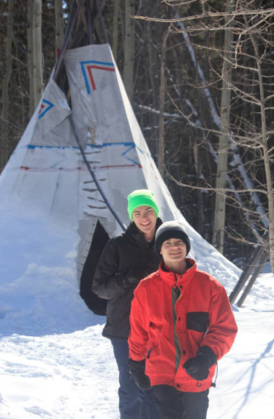 due ragazzi caucasici al campo di tipi invernale - north american tribal culture teepee winter canada foto e immagini stock