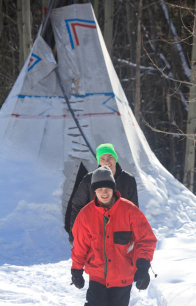 due ragazzi caucasici al campo di tipi invernale - north american tribal culture teepee winter canada foto e immagini stock
